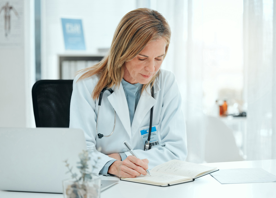 Foto de uma médica madura sentada sozinha em sua clínica e escrevendo notas
