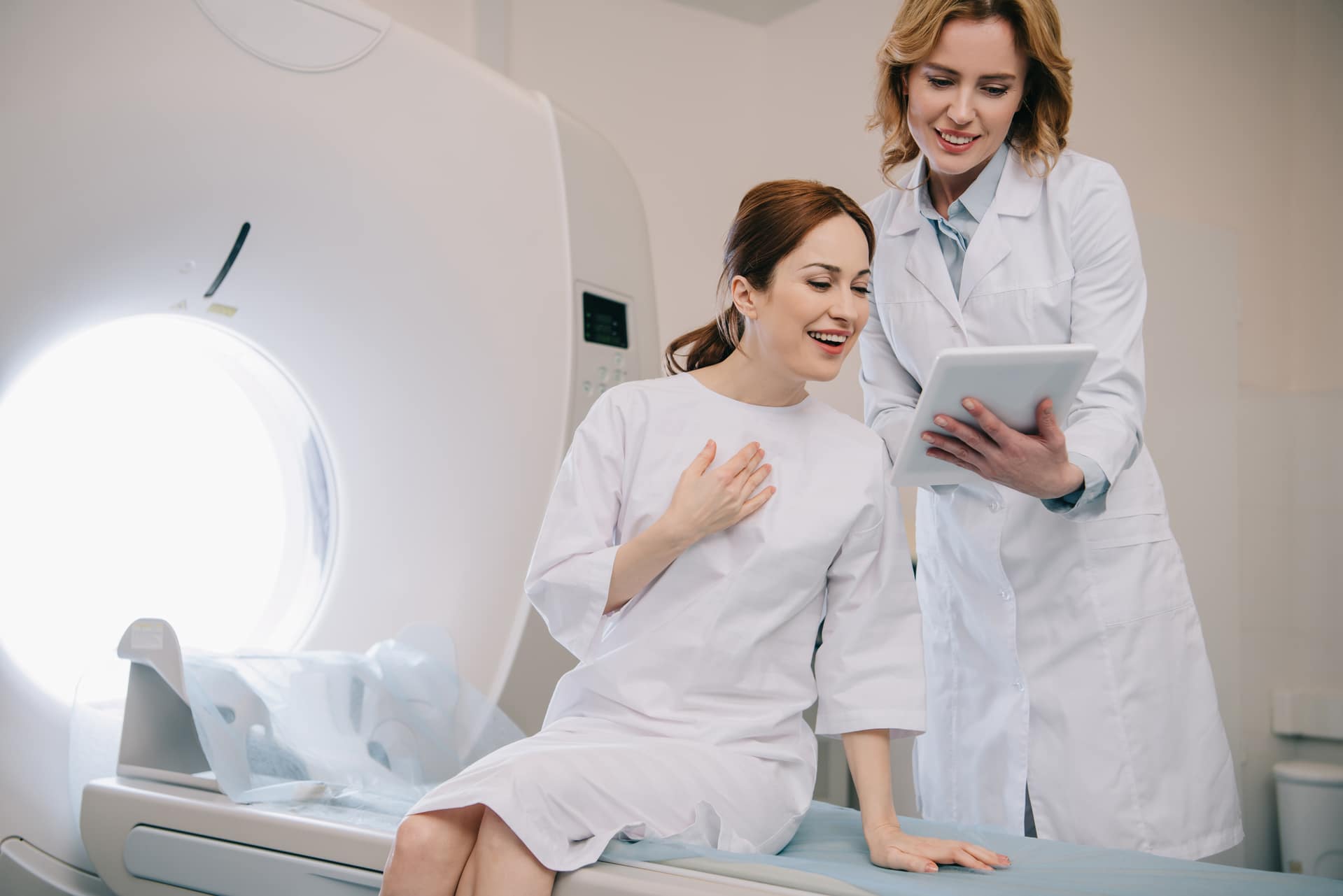 radiologista sorridente mostrando diagnóstico de raio-x para paciente feliz sentado na cama do tomógrafo